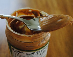 Spoon with peanut butter resting on the jar of peanut butter - Not Paleo Diet friendly